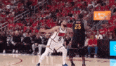 two basketball players are playing a game of basketball in front of a crowd in a stadium .