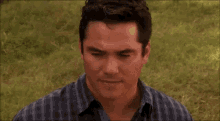 a man in a plaid shirt is standing in a field of grass looking down .