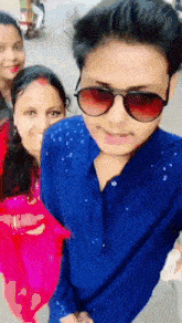 a man wearing sunglasses and a blue shirt poses for a photo with two women