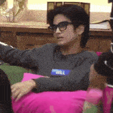a man wearing glasses and a name tag that says will is sitting on a pink pillow