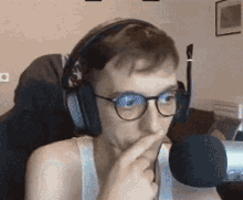 a young man wearing headphones and glasses is talking into a microphone .