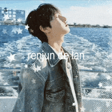 a man in a denim jacket stands in front of a body of water with the name renjun de lan written on the bottom