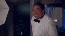 a man in a tuxedo and bow tie stands in front of a camera