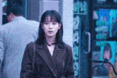 a woman in a plaid coat stands in front of a store with a sign that says ' a ' on it