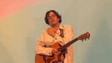 a man wearing glasses is playing a guitar and covering his mouth .