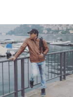 a man leaning on a railing near a body of water with boats in the background