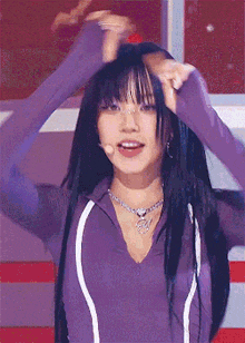 a woman with long black hair is wearing a purple shirt and a necklace while standing on a stage .