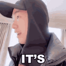 a man wearing a hat and a hoodie with the words `` it 's '' on it .