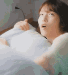 a woman is laying in bed with a pillow and a blanket and making a funny face .