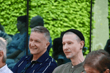 a group of men are sitting in front of a green wall and smiling