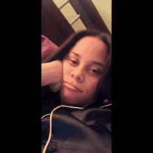 a woman wearing headphones lays on a bed with her hand on her face