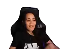 a woman is sitting in a gaming chair and smiling while holding a cell phone .