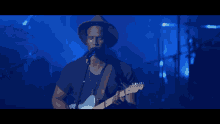 a man in a hat singing into a microphone while playing a guitar