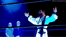 a wrestler in a white robe is standing in a wrestling ring with his arms outstretched .