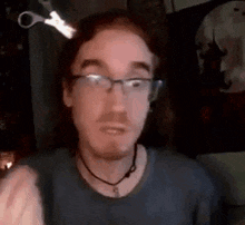 a man wearing glasses and a choker is holding a pair of scissors in his head .