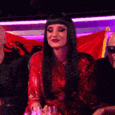 a woman in a red dress is sitting at a table in front of a flag .