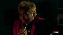 a man in a red vest is singing into a microphone with a bull logo in the corner
