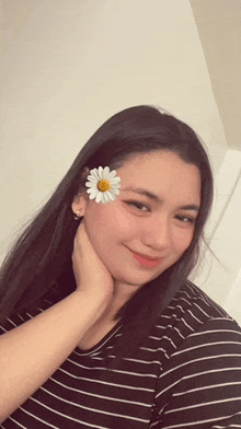 a woman wearing a black and white striped shirt has a white flower in her hair .