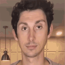 a close up of a man 's face with a lamp hanging from the ceiling in the background
