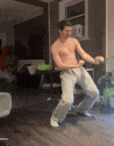 a shirtless man dancing in a living room with a plant in the background