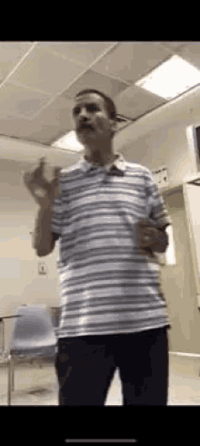 a man in a striped shirt is standing in a room with his hands up .