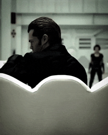a man in a black jacket sits on a couch