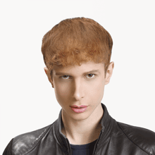 a young man with red hair is wearing a leather jacket