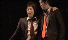 two men in suits and ties are standing next to each other on a stage in a dark room .