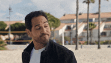 a man with a beard is standing on a beach making a funny face