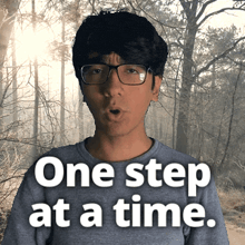 a man with glasses says one step at a time in front of a forest