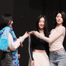 three women are standing next to each other and one has a blue scarf around her neck