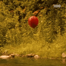a red balloon is floating in the air near a body of water with the hbo logo in the background