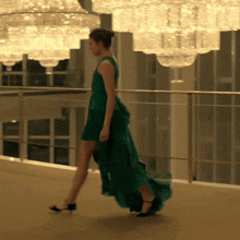 a woman in a long green dress is walking down a hallway