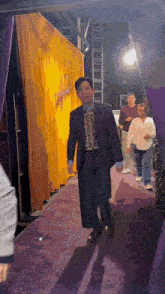 a man in a suit walks on a purple carpet