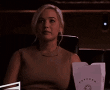 a woman is sitting in a theater holding a bucket of popcorn