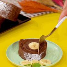 a person is using a fork to cut a chocolate roll with bananas on it