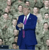 donald trump is standing in front of a crowd of soldiers applauding