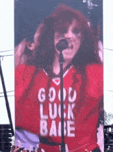 a woman singing into a microphone wearing a red jersey that says good luck babe