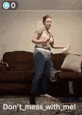 a woman is standing in front of a couch holding a pillow and a remote control .