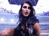 a woman in a black vest is standing in a wrestling ring and looking at the camera .