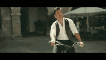 a man in a vest and white shirt is riding a bicycle