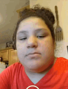 a woman in a red shirt looks at the camera with a fork hanging on the wall behind her