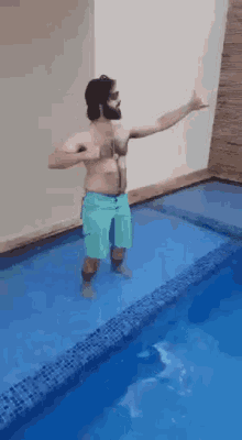 a man without a shirt is standing in a swimming pool with his arms outstretched
