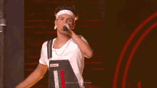 a young man wearing overalls and a headband is singing into a microphone on a stage .