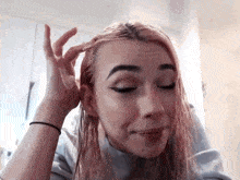 a woman with pink hair is touching her hair with her hand