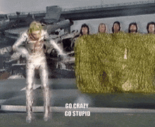 a man in a silver suit is standing in front of a group of people with the words go crazy go stupid written below him