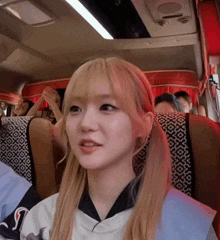 a girl with blonde hair is sitting in a bus with the letter t on the back of her shirt