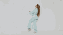 a woman in a light blue adidas suit is dancing against a white background .