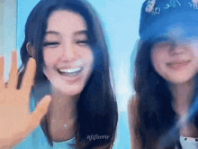 two young women are standing next to each other and smiling . one of the girls is wearing a blue hat .