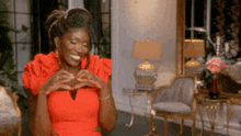 a woman in a red dress is smiling and making a heart with her hands .